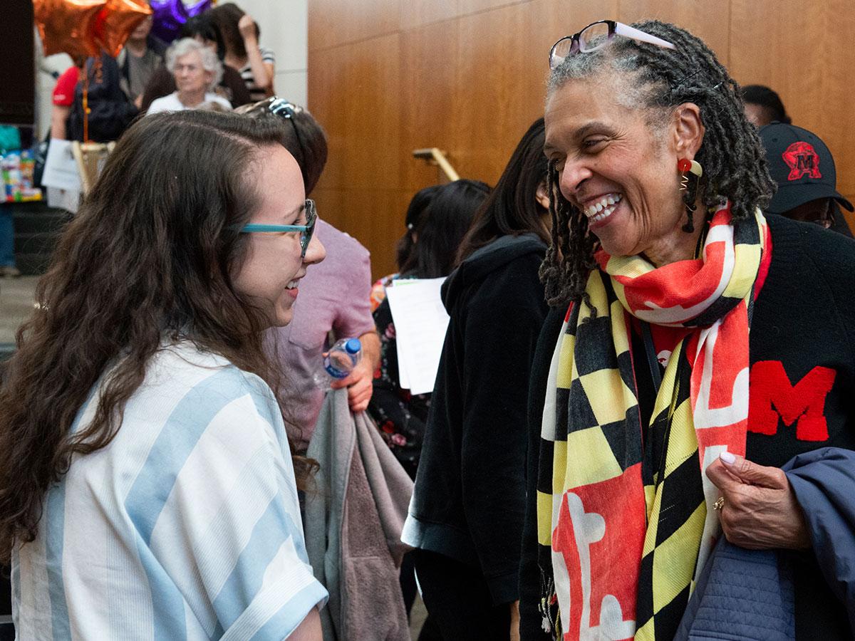 Alumni wearing a Maryland flag scarf and laughing with a student